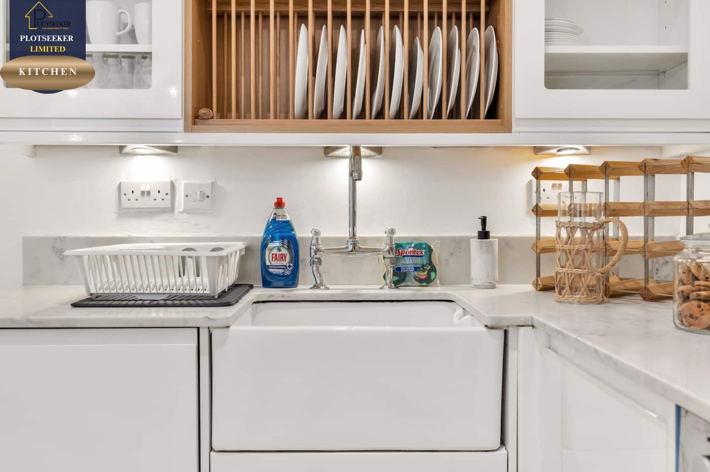 A kitchen with a white countertop, a sink, a dish rack, and a bottle of Fairy dish soap.