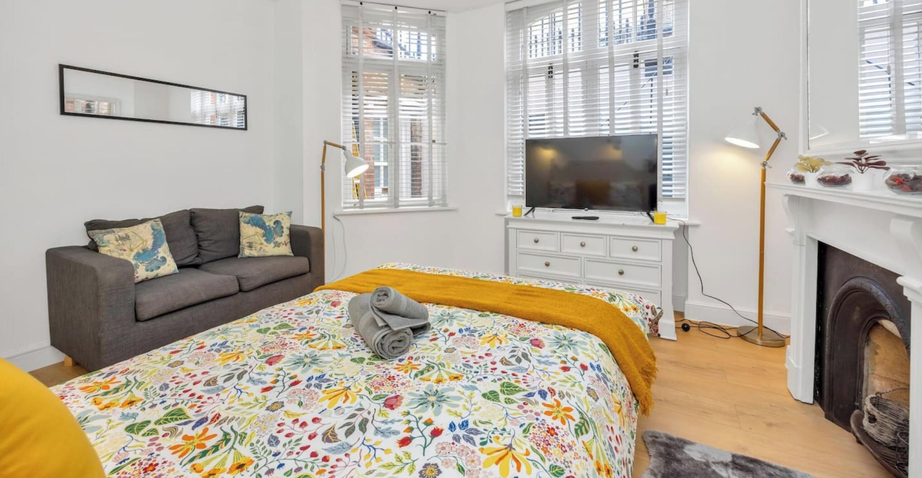 A bedroom with a bed, a television, a sofa, and a fireplace.
