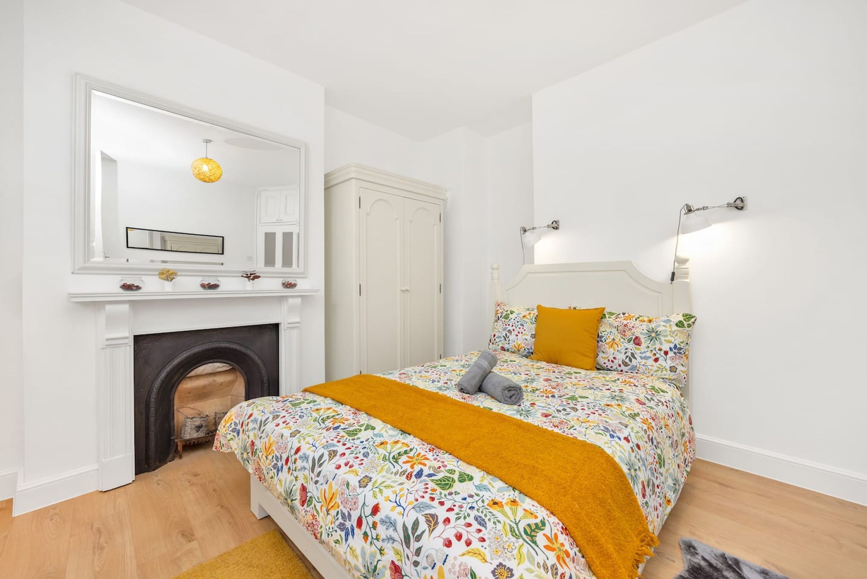Ein Schlafzimmer mit einem Bett, einem Kamin, einem Spiegel und einer Wandleuchte.