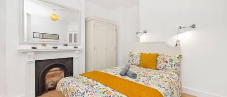 Ein Schlafzimmer mit einem Bett, einem Kamin, einem Spiegel und einer Wandleuchte.