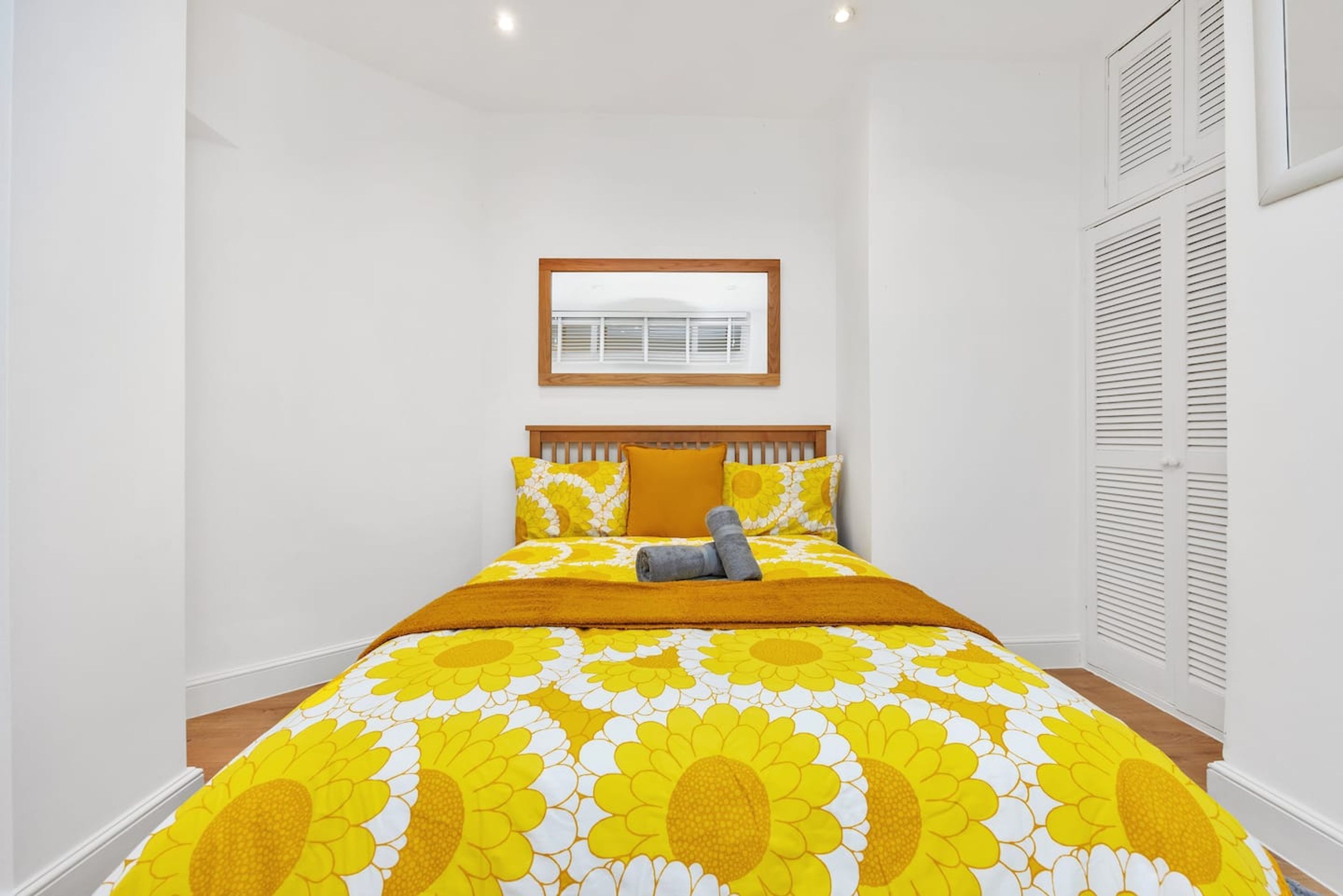 A bedroom with a bed, a framed picture on the wall, and a window with blinds.
