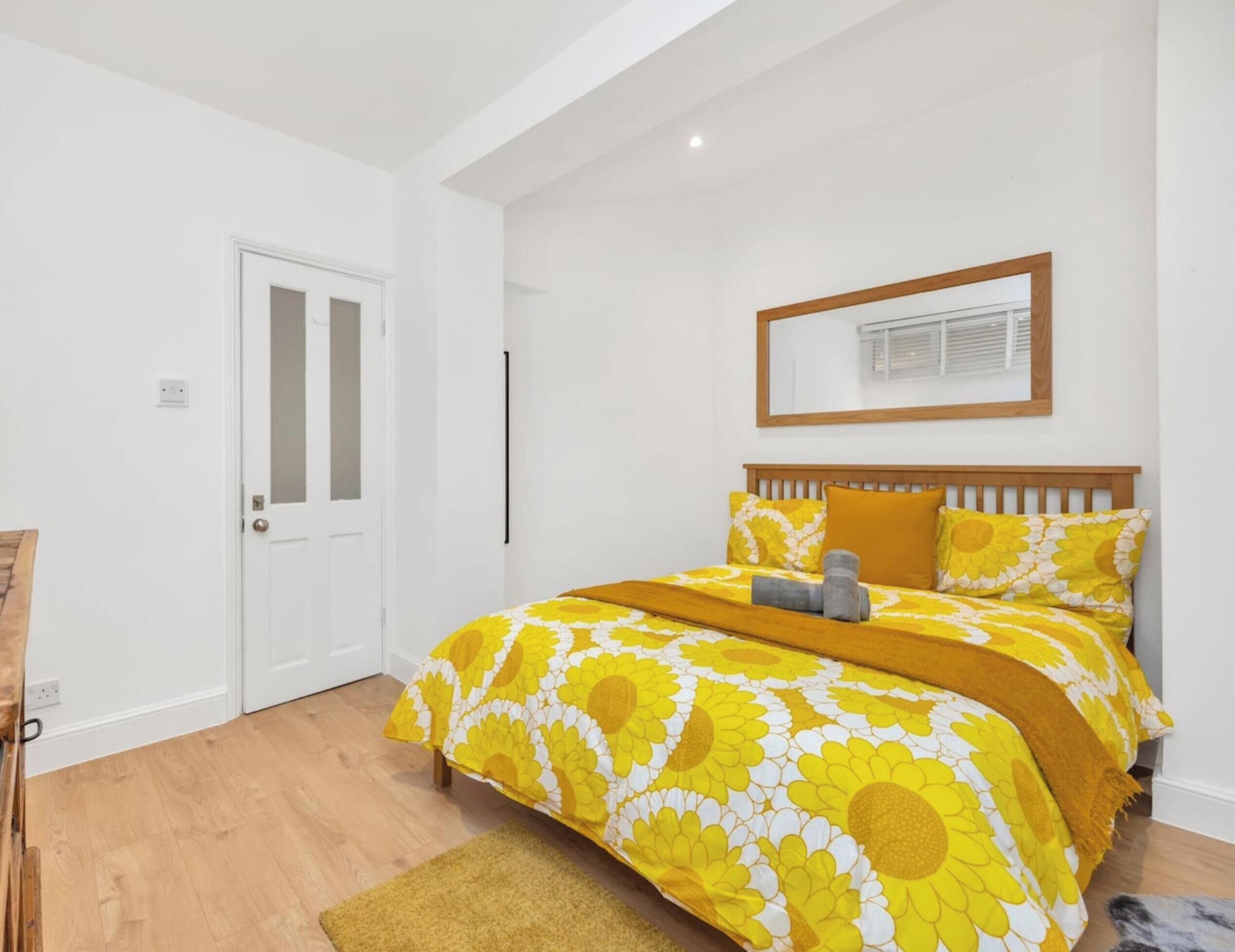 A bedroom with a bed, a door, a window with blinds, and a wooden floor.