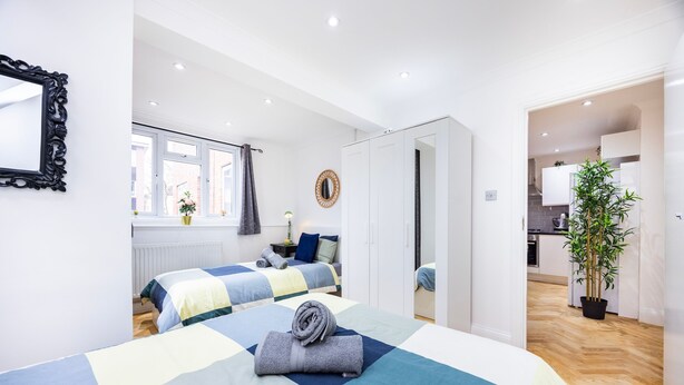 A modern bedroom with a large bed, a mirror, and a view into the kitchen. - 2 Bedroom Charming Family Apartment (London)