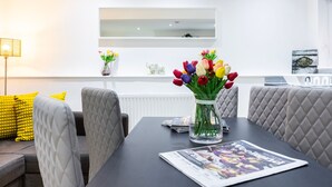 A modern dining area with a dark table, cushioned chairs, and a vase of tulips. - 2 Bedroom Charming Family Apartment (London)