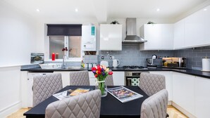 A modern kitchen with white cabinets, a black countertop, and a dining area with a black table and cushioned chairs. - 2 Bedroom Charming Family Apartment (London)