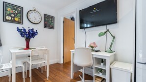 Ein moderner, gut beleuchteter Raum mit einem weißen Schreibtisch, einem Stuhl und einem an der Wand befestigten Fernseher.