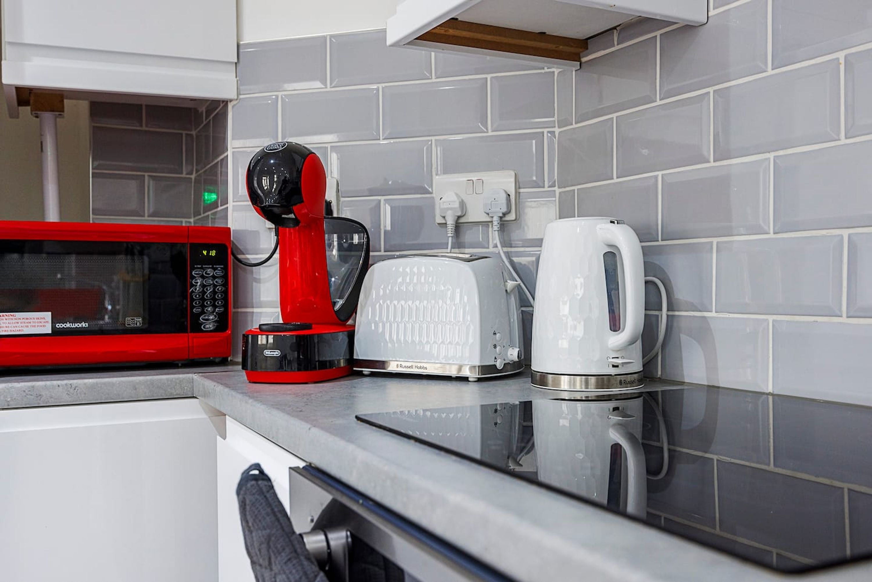 Een keuken met een rode magnetron, een broodrooster en een waterkoker op een aanrecht.
