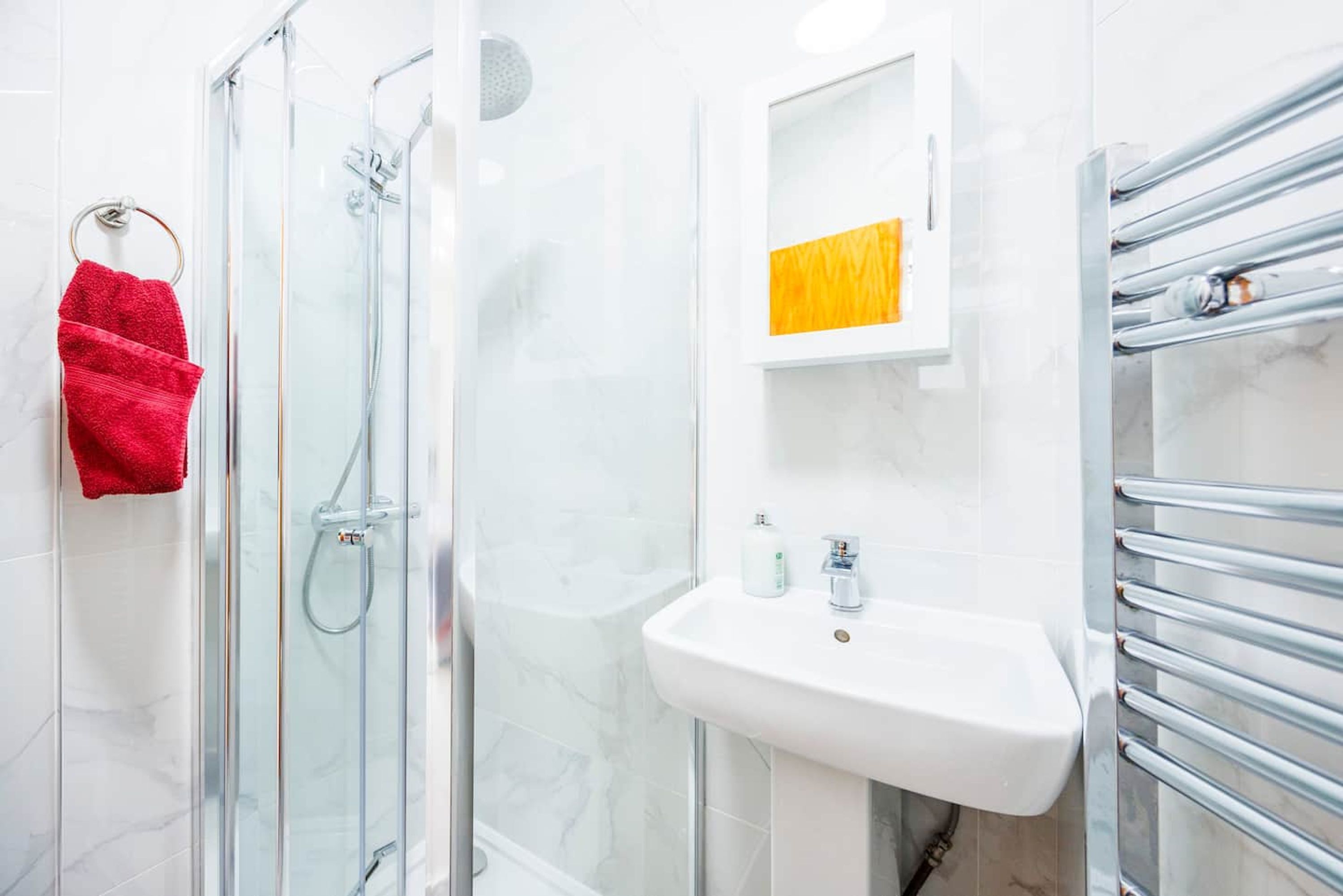 Une salle de bain avec une douche à parois de verre, un lavabo blanc et un porte-serviettes.