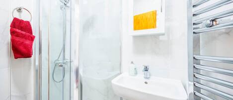 Une salle de bain avec une douche à parois de verre, un lavabo blanc et un porte-serviettes.