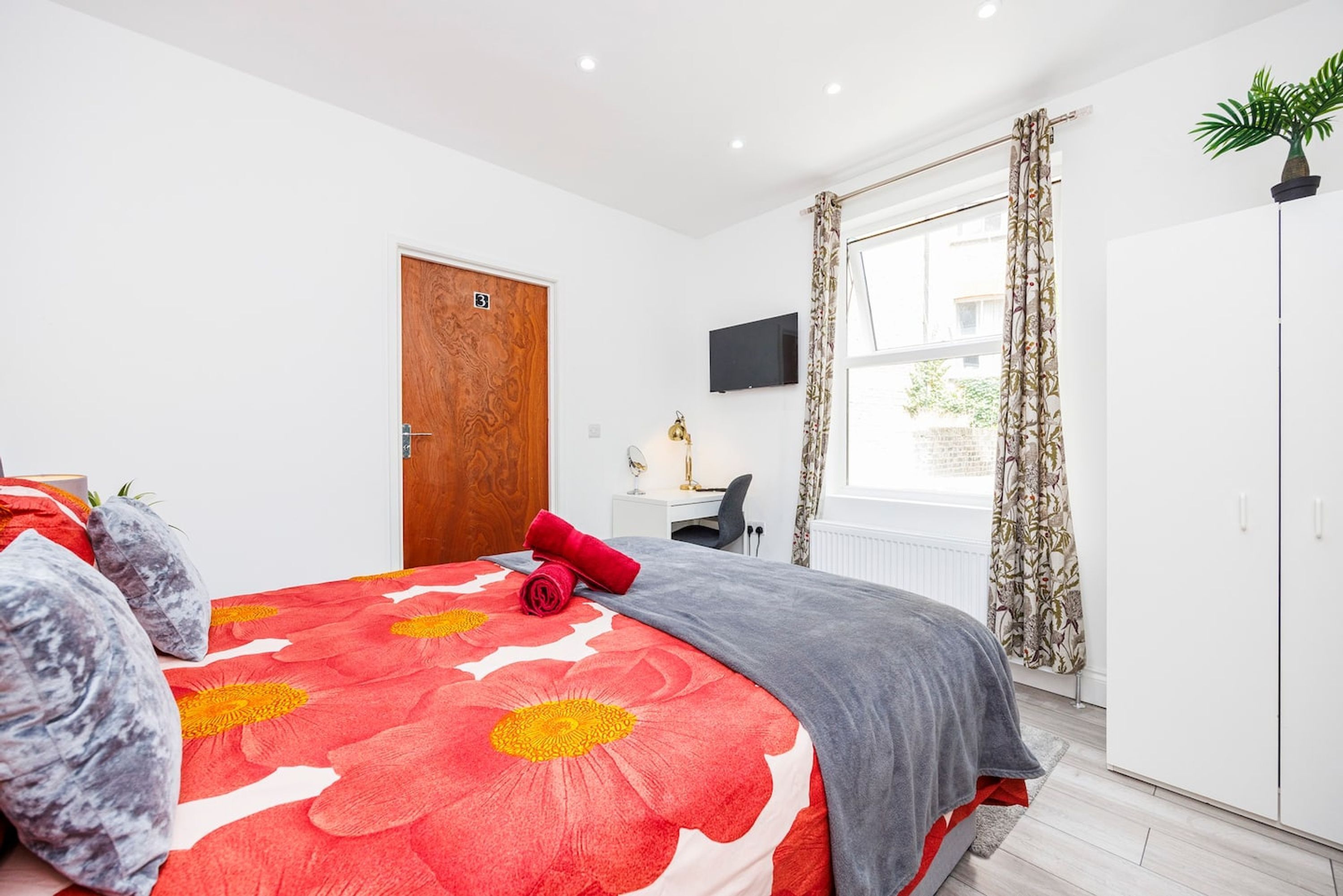 A bedroom with a large bed, a desk, a TV, and a wardrobe.