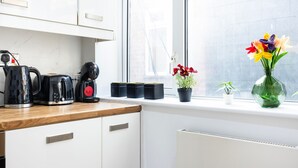 A kitchen with white cabinets, a wooden countertop, a kettle, a coffee maker, and a window with a view of the outside. - 2 Bedroom Charming Magnificent Flat (London)