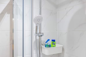 A shower area with a handheld showerhead, a glass door, and a white shelf with two bottles of Radox and a blue container.