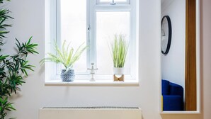 A window with two potted plants, a white radiator below, and a clock on the wall. - 2 Bedroom Charming Magnificent Flat (London)