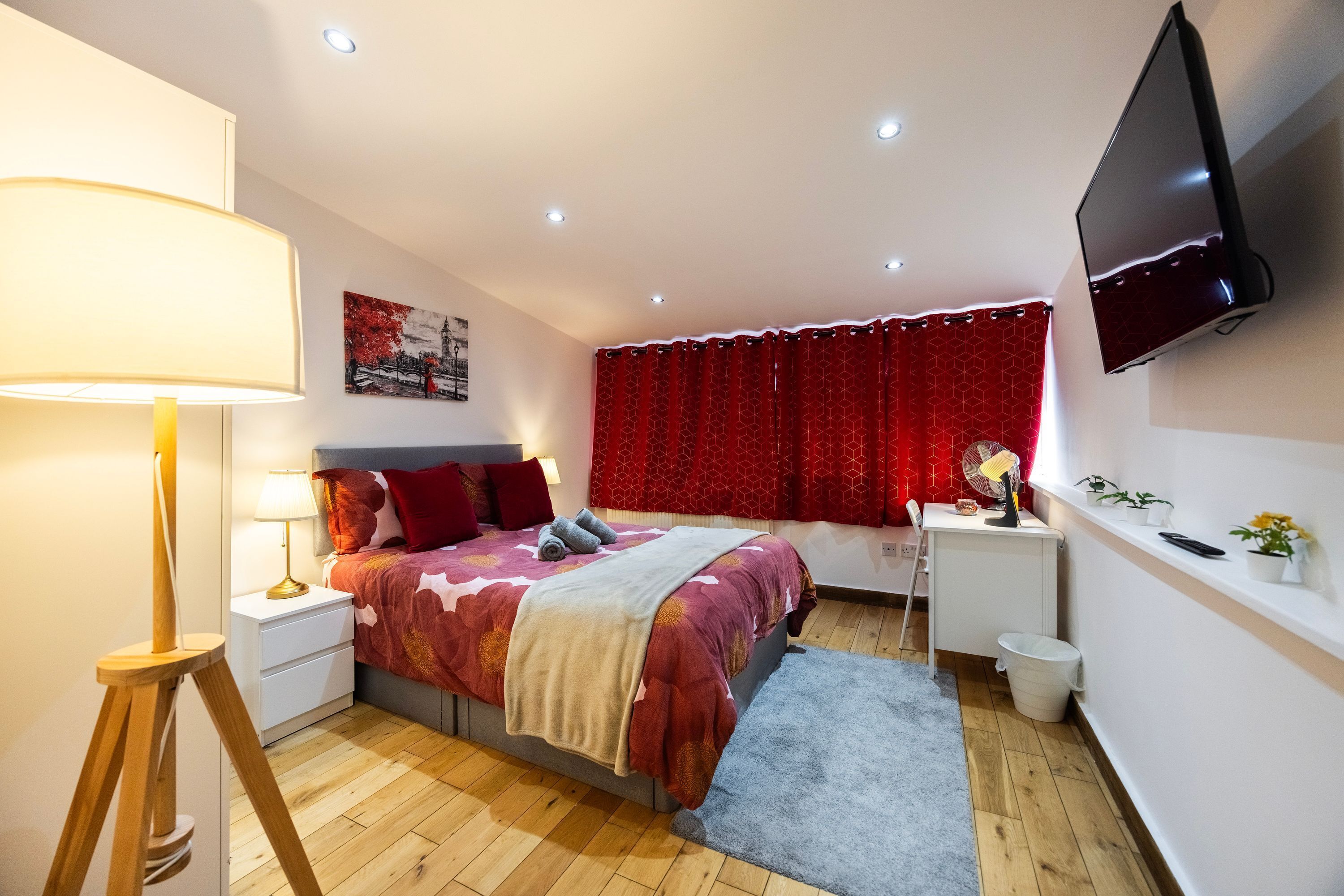 A bedroom with a bed, bedside table, lamp, TV, and a small desk with a chair.