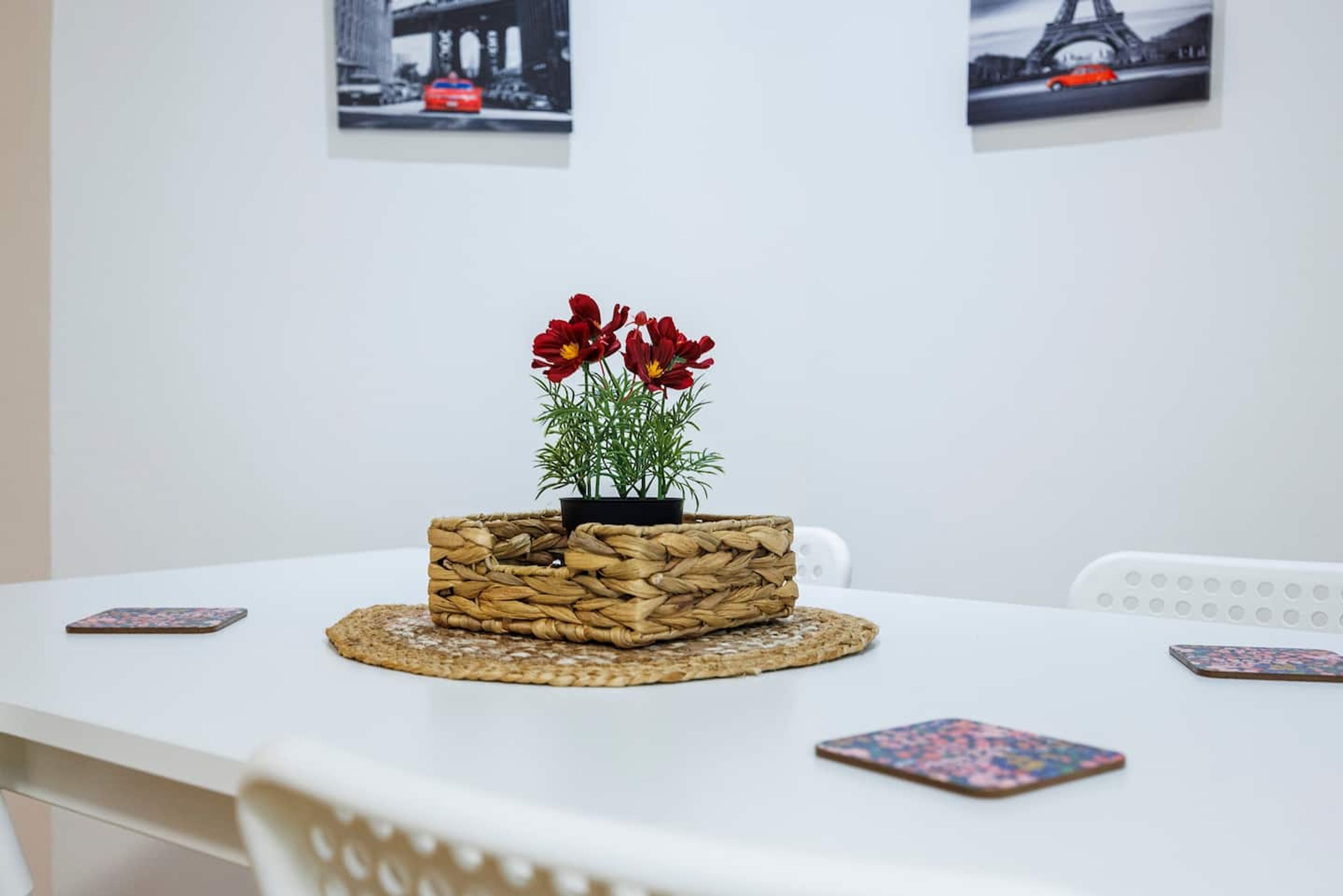 A white table with a woven basket containing red flowers and a small plant.
