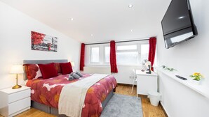 A bedroom with a bed, bedside table, lamp, TV, window with curtains, and a desk with a chair. - 2 Bedroom Charming Magnificent Flat (London)