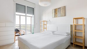 Een slaapkamer met een groot bed, een houten stoel, een bureau, een hanglamp en een schilderij aan de muur.