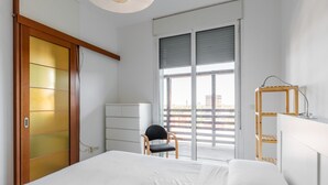 Een slaapkamer met een bed, een stoel, een bureau en een raam met uitzicht.