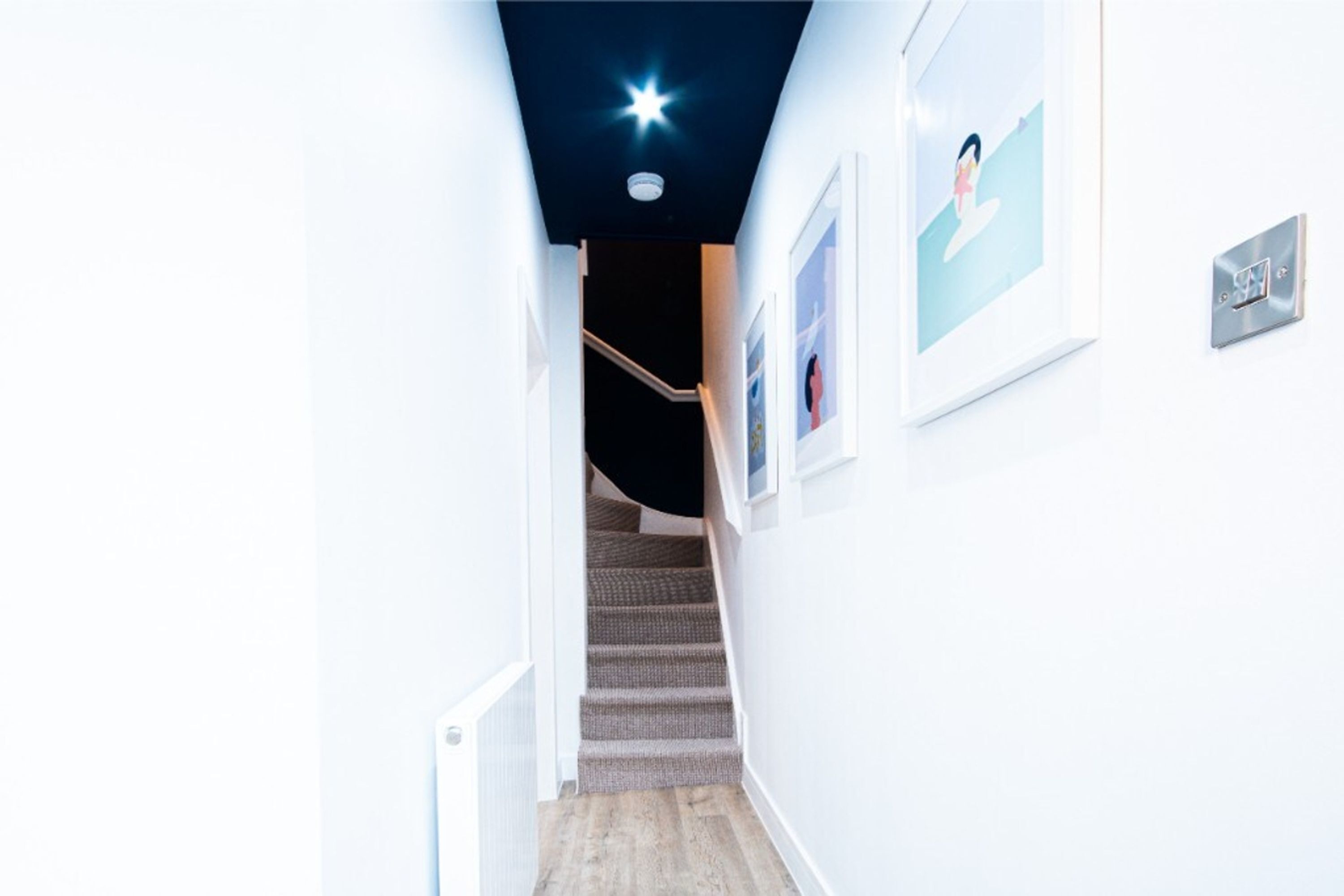 A modern hallway with a staircase leading to a dark room.
