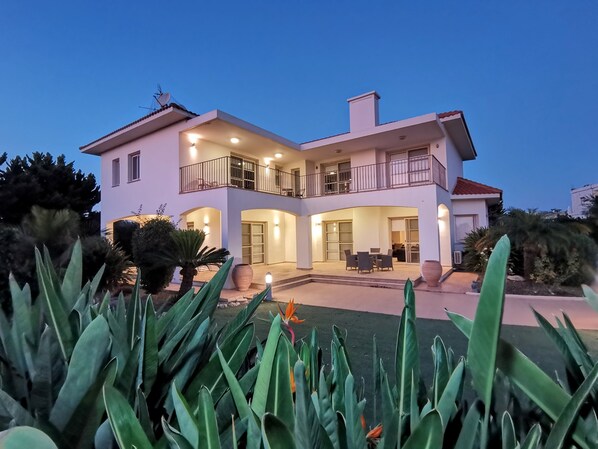 A two-story house with a balcony, a patio with outdoor furniture, and a well-maintained garden.