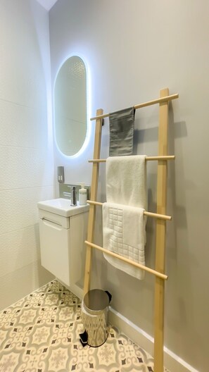 Casa de banho com pia branca, espelho, porta-toalhas e chão estampado.