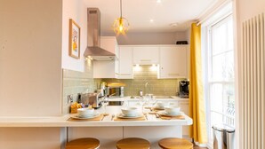 A modern kitchen with white cabinets, a central island with stools, and a yellow curtain by the window. - Old Town Trinity Apt No 3 By Adliv (Margate)
