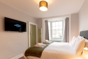 A hotel room with a bed, a television displaying 'amazon prime video', a window with curtains, and a radiator.