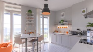A modern kitchen with white cabinets, a central island, and a dining area with a white table and chairs. - Seaview Apt Turner Contemporary Margate By Adliv (Margate)