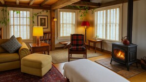 A cozy room with a sofa, armchair, and ottoman, a fireplace, and large windows with blinds. - Magical Post and Beam Loft Downtown Newport (Newport)