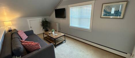 A living room with a sofa, coffee table, and a TV mounted on the wall.