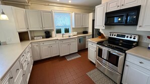 A modern kitchen with white cabinets, a black stove, and a window with blinds.