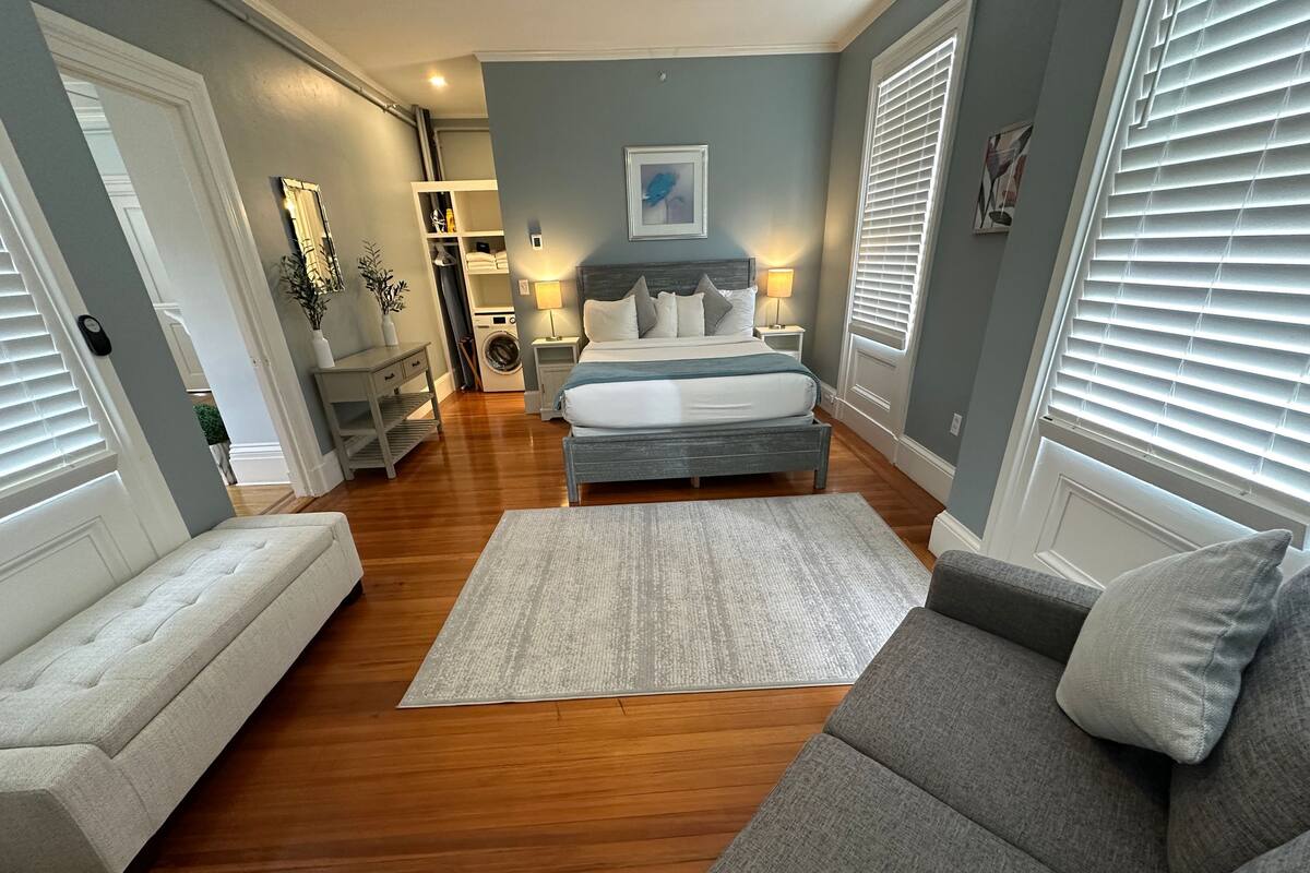 A bedroom with a bed, bedside tables, a nightstand, a dresser, a bench, and a window with blinds.