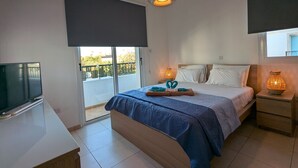 A bedroom with a bed, a TV, a balcony, and a hanging light fixture. - Amelia Villa With Private Pool Wifi BBQ (Paralimni)