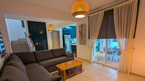 A modern living room with a sofa, a wooden coffee table, and a staircase leading to a kitchen and dining area. - Amelia Villa With Private Pool Wifi BBQ (Paralimni)