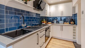 A modern kitchen with blue tiles, white cabinets, and a black stove.