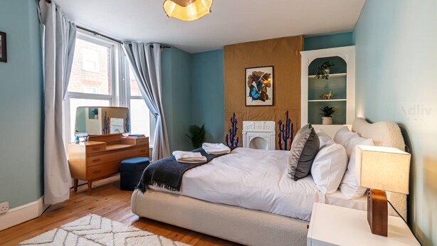 A bedroom with a bed, bedside table, lamp, dresser, and a window with curtains.