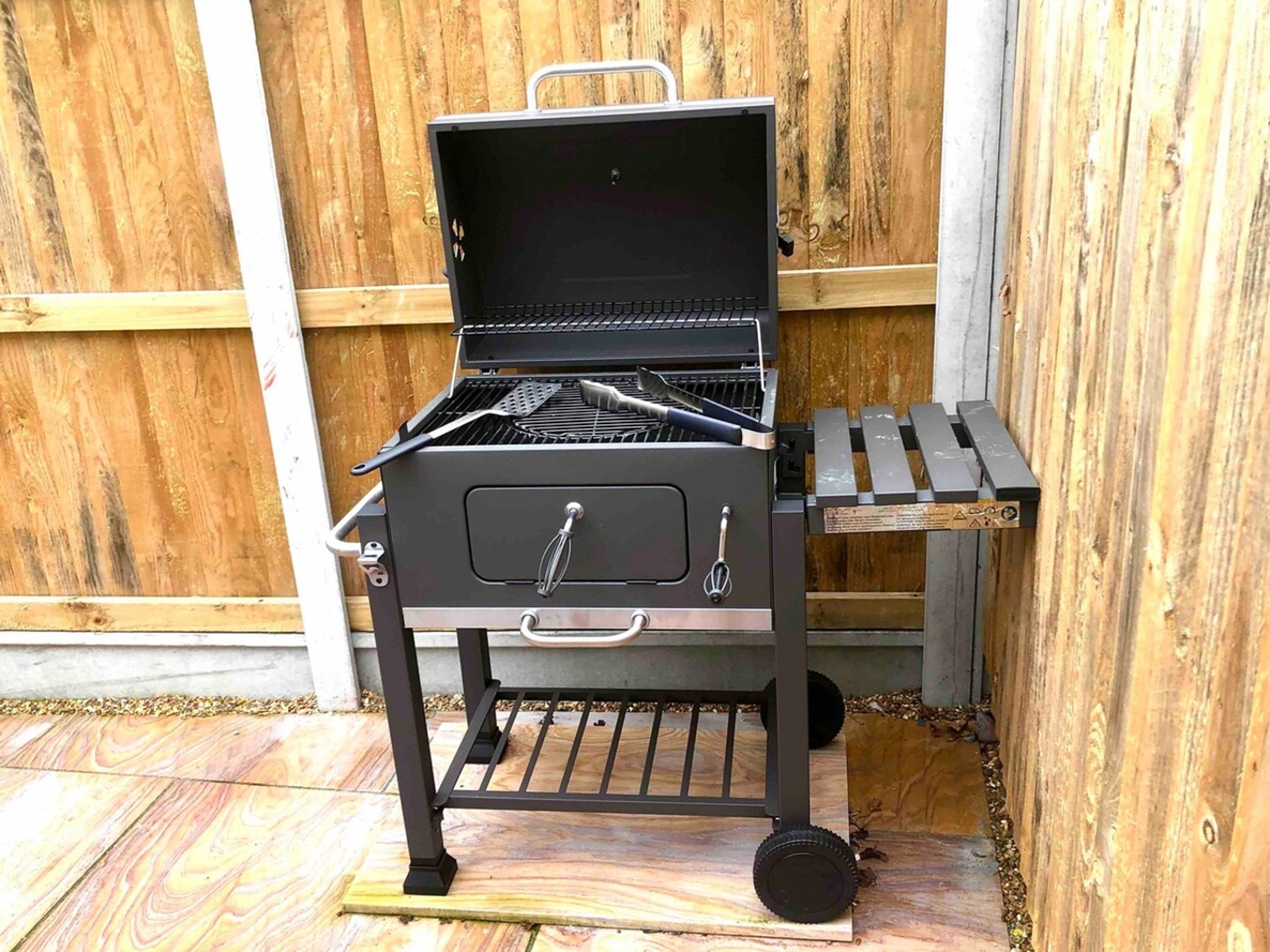 A portable grill with a handle, a lid, and a side storage compartment.