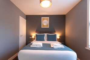 Ein Hotelzimmer mit einem Bett, zwei Nachttischen, einem Wandbild und einem Fenster mit Jalousien.
