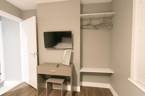 Une petite pièce bien éclairée, avec un bureau, un miroir et une étagère suspendue.