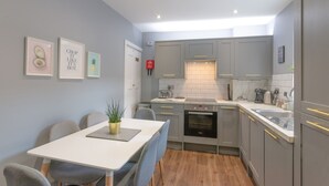 Eine moderne Küche mit grauen Schränken, einer weißen Arbeitsplatte und einem eingebauten Backofen. Ein Esstisch mit Stühlen und eine kleine Pflanze stehen auf dem Tisch.