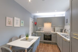 Eine moderne Küche mit grauen Schränken, einer weißen Arbeitsplatte und einem eingebauten Backofen. Ein Esstisch mit Stühlen und eine kleine Pflanze stehen auf dem Tisch.