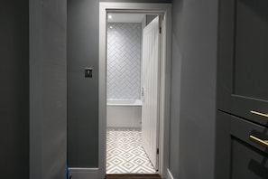 Un couloir étroit mène à une salle de bain dont le mur est décoré d’un motif en chevrons et le sol d’un motif géométrique.