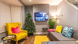 Ein Wohnzimmer mit einem gelben Sessel, einem grauen Sofa, einem Weihnachtsbaum und einem an der Wand montierten Flachbildfernseher.