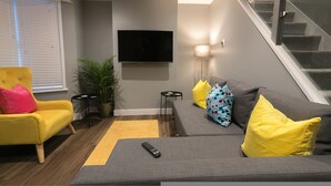 Ein modernes Wohnzimmer mit grauem Sofa, gelben Kissen, einem gelben Sessel, einem Flachbildfernseher und einer Treppe.