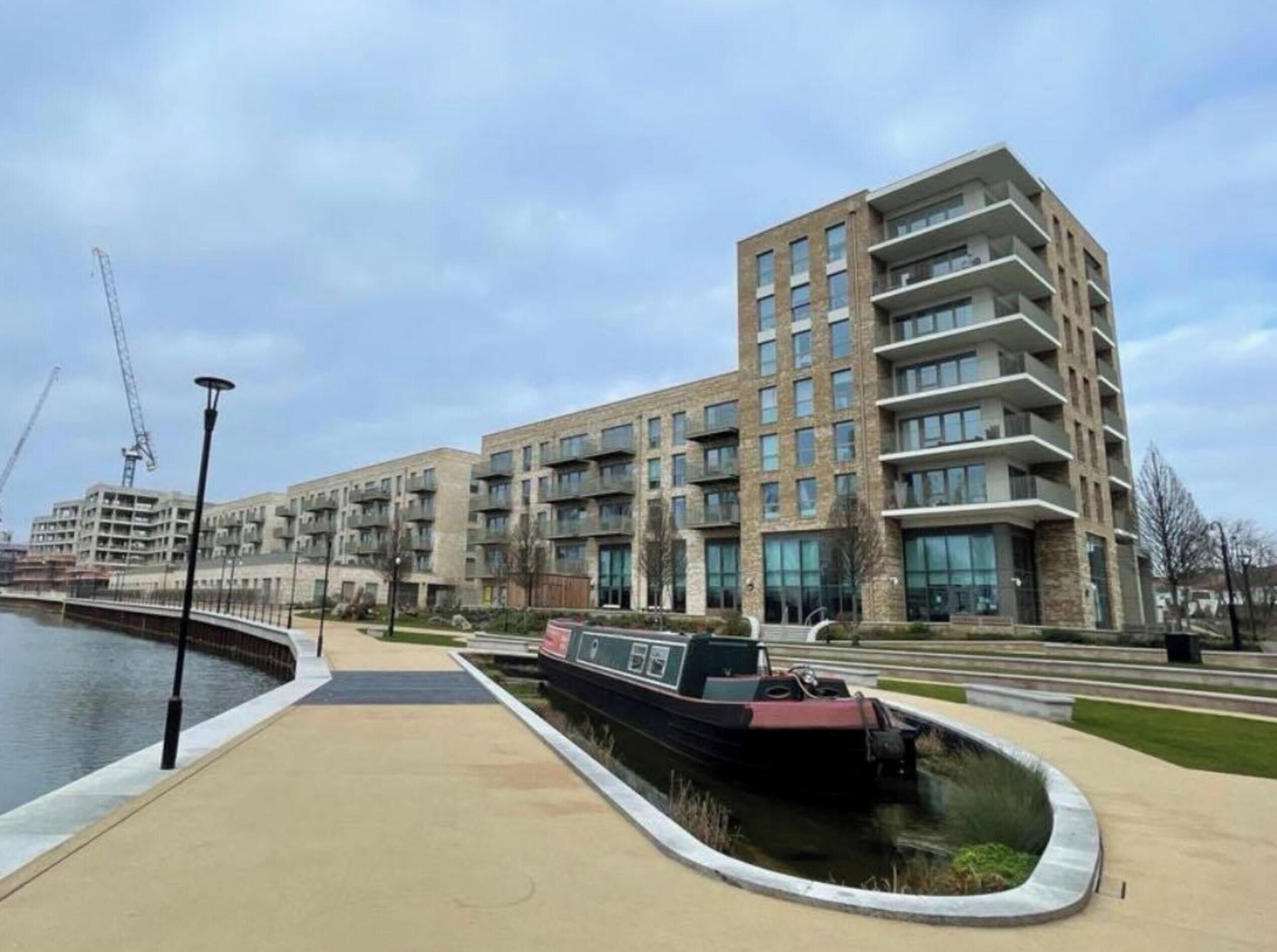 A modern apartment building with multiple balconies, a canal, and a pedestrian walkway.