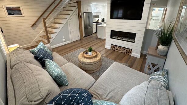 Ein modernes Wohnzimmer mit Sofa, Couchtisch, Kamin, Fernseher, Küchenzeile und Treppe.