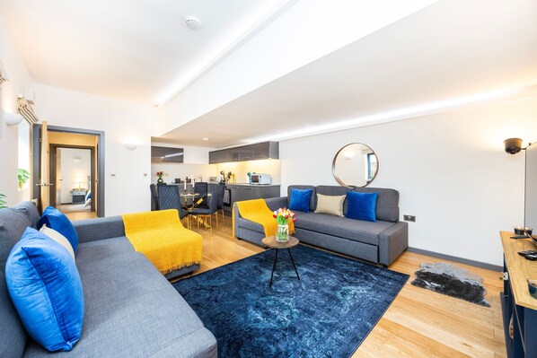Una sala de estar moderna con un sofá gris, almohadas azules, una manta amarilla y una alfombra azul.