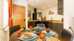 A dining area with a round table set for breakfast, a kitchen in the background, and a wall with the word "SEA". - Dreamland Cottage Margate by Adliv (Margate)