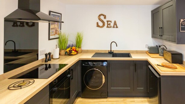 A modern kitchen with a built-in dishwasher, a black stove, and a wooden countertop. - Dreamland Cottage Margate by Adliv (Margate)