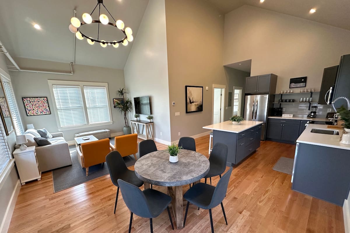 A modern kitchen with a central island, a dining area with a round table, and a living space with a sofa and a TV.